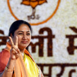 delhi cm rekha gupta showing victory sign with bjp logo behind her