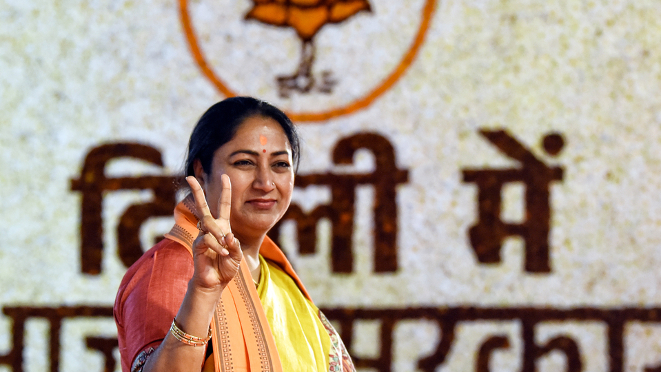 delhi cm rekha gupta showing victory sign with bjp logo behind her